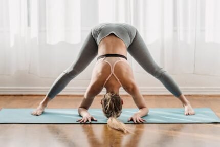 Fit female in sportswear doing yoga in Prasarita Padottanasana pose with bent back on mat in light room